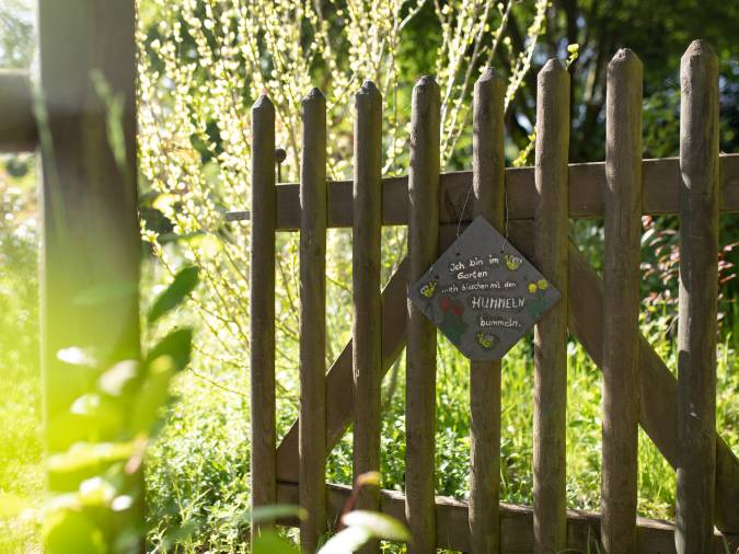 Holzzaun mit einem Schild im Garten des Klinikum Schloss Lütgenhof, der die harmonische Verbindung zur Natur zeigt.